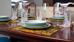 A dining table set with plates, glasses, and cutlery, with a patterned placemat and a wooden table. - 3-Bedroom Apartment in Tema - Chez Akwasi (Tema)