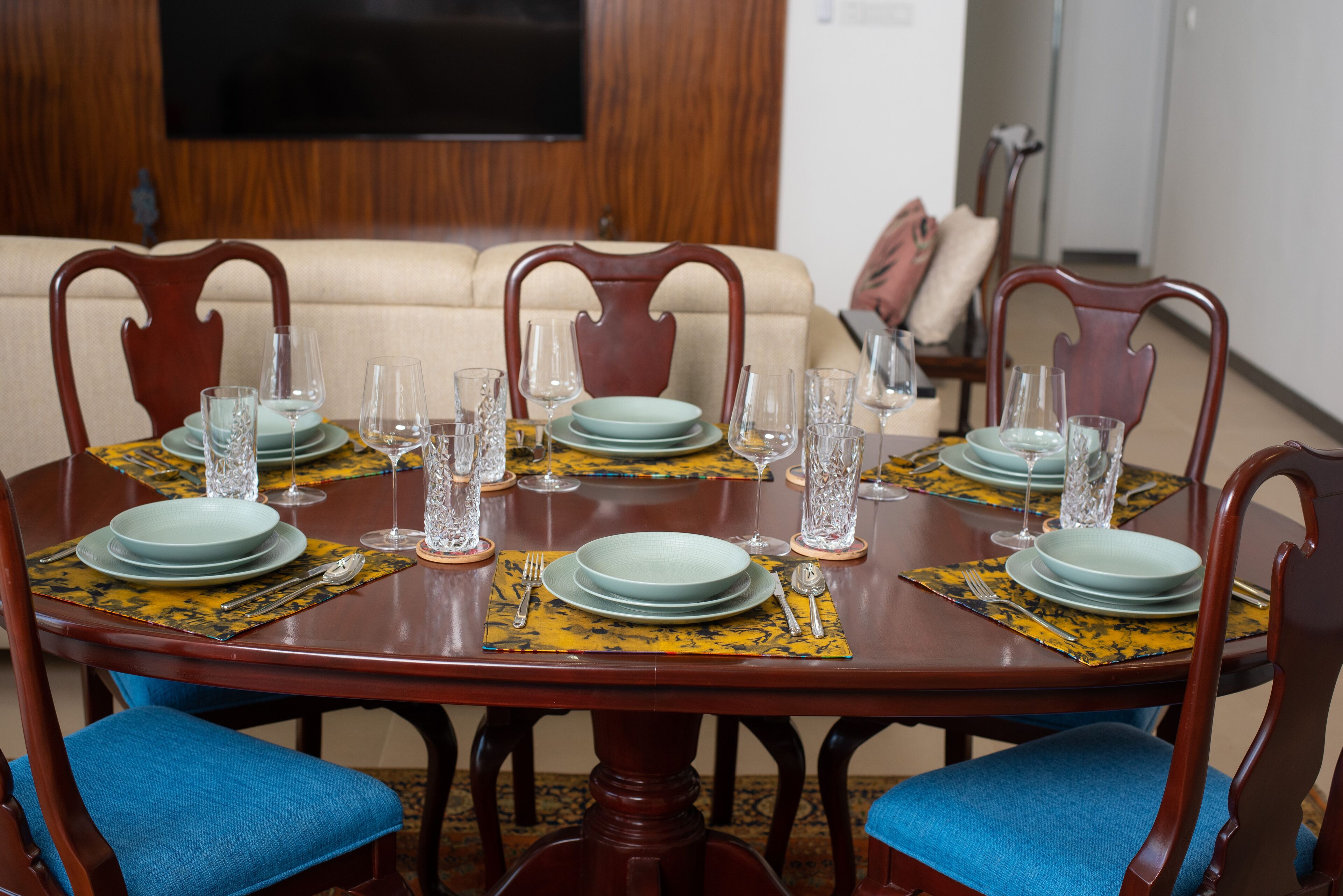 A dining table set with plates, glasses, and cutlery, surrounded by chairs with blue cushions.