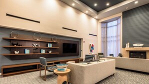 Un moderno salón de hotel con televisión de pantalla plana, asientos cómodos, chimenea y estantería.