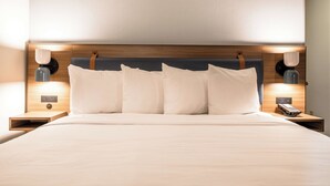 Una cama bien hecha con cabecera de madera, dos mesitas de noche con lámparas y un teléfono sobre una de ellas.