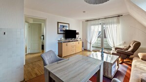 A modern living room with a dining table, two chairs, a sofa, a television, and a window with curtains.