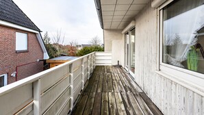 A wooden deck with a railing, a brick building, and a white building with a window.