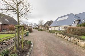Une rue résidentielle bordée de maisons, avec un trottoir dallé et un mur en pierre.