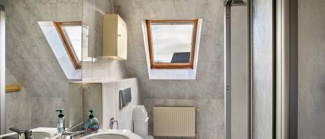 Et badeværelse med ovenlys, toilet, vask og spejl.
