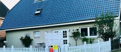 Un bâtiment avec un toit recouvert de tuiles bleues, une clôture blanche en bois et une enseigne.