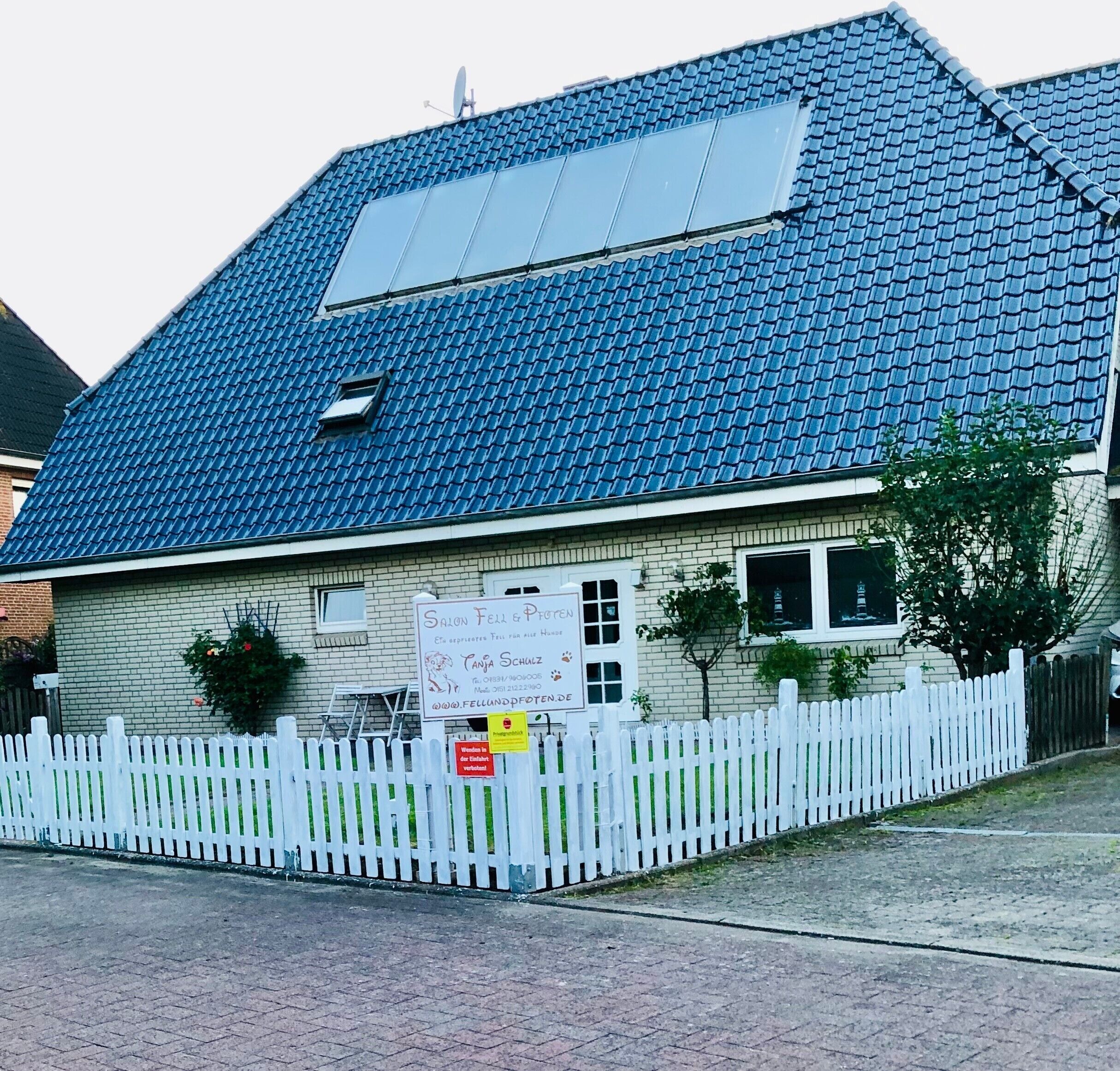 A building with a blue tiled roof, a white picket fence, and a signboard.