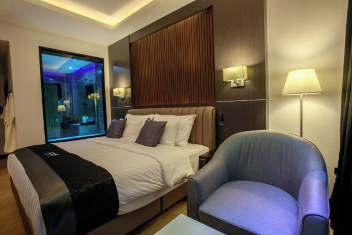 Una habitación de hotel moderna con una cama grande, un área de descanso y vistas a una piscina a través de un muro de vidrio.