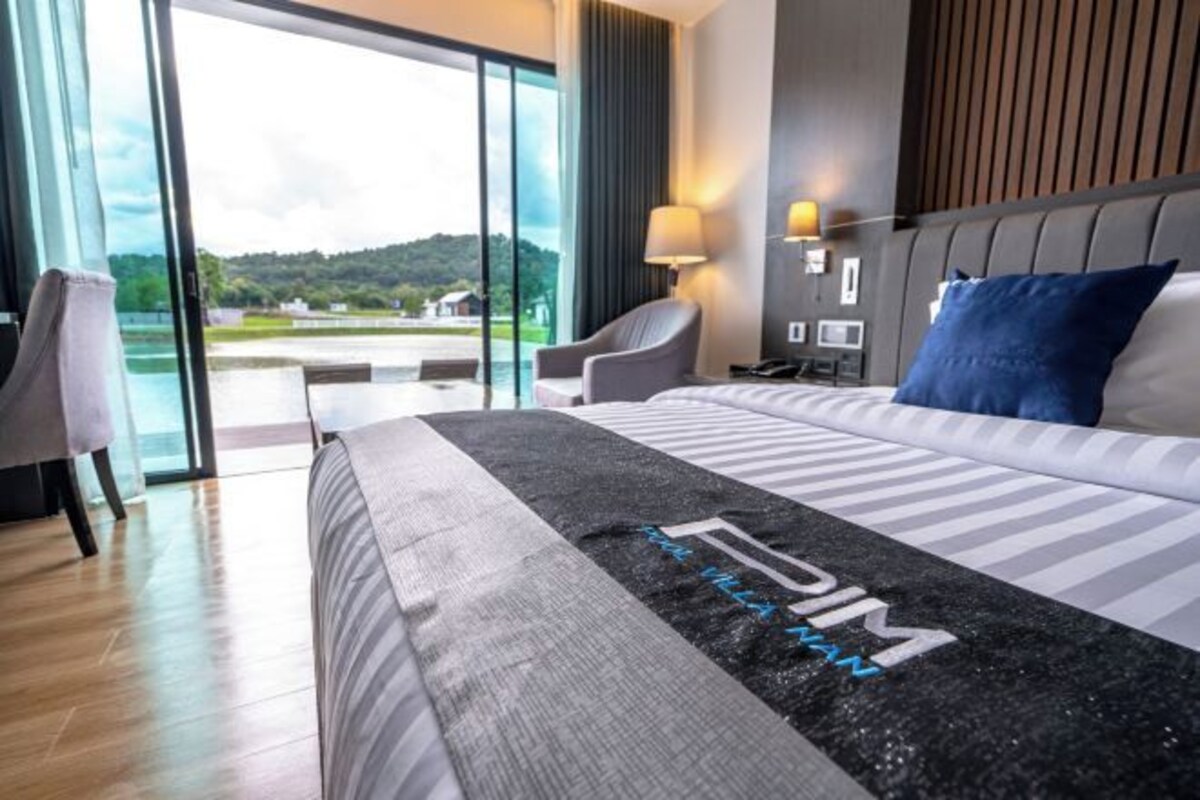 Habitación de hotel moderna con una cama grande, una silla, un escritorio y vistas a un paisaje verde a través de la puerta de vidrio.