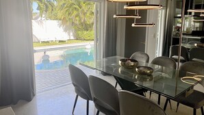 Een moderne eethoek met een glazen tafel, grijze stoelen en uitzicht op een zwembad.