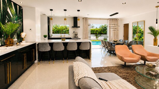 Een moderne keuken met een centraal eiland, barkrukken en een eethoek met oranje stoelen.