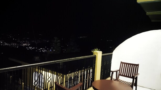 Un balcon avec une table et deux chaises, une balustrade et une vue sur la ville la nuit.