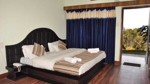 Un lit bien fait, recouvert d’une couvre-lit à motifs, avec un téléphone sur la table de chevet et une vue sur l’extérieur par une fenêtre ornée de rideaux bleus.