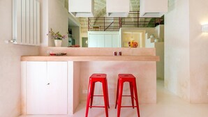 A compact kitchen with a central island, two red stools, and a white refrigerator.