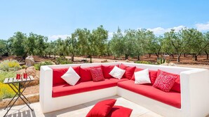 A white sectional sofa with red cushions in an outdoor setting with a view of olive trees.