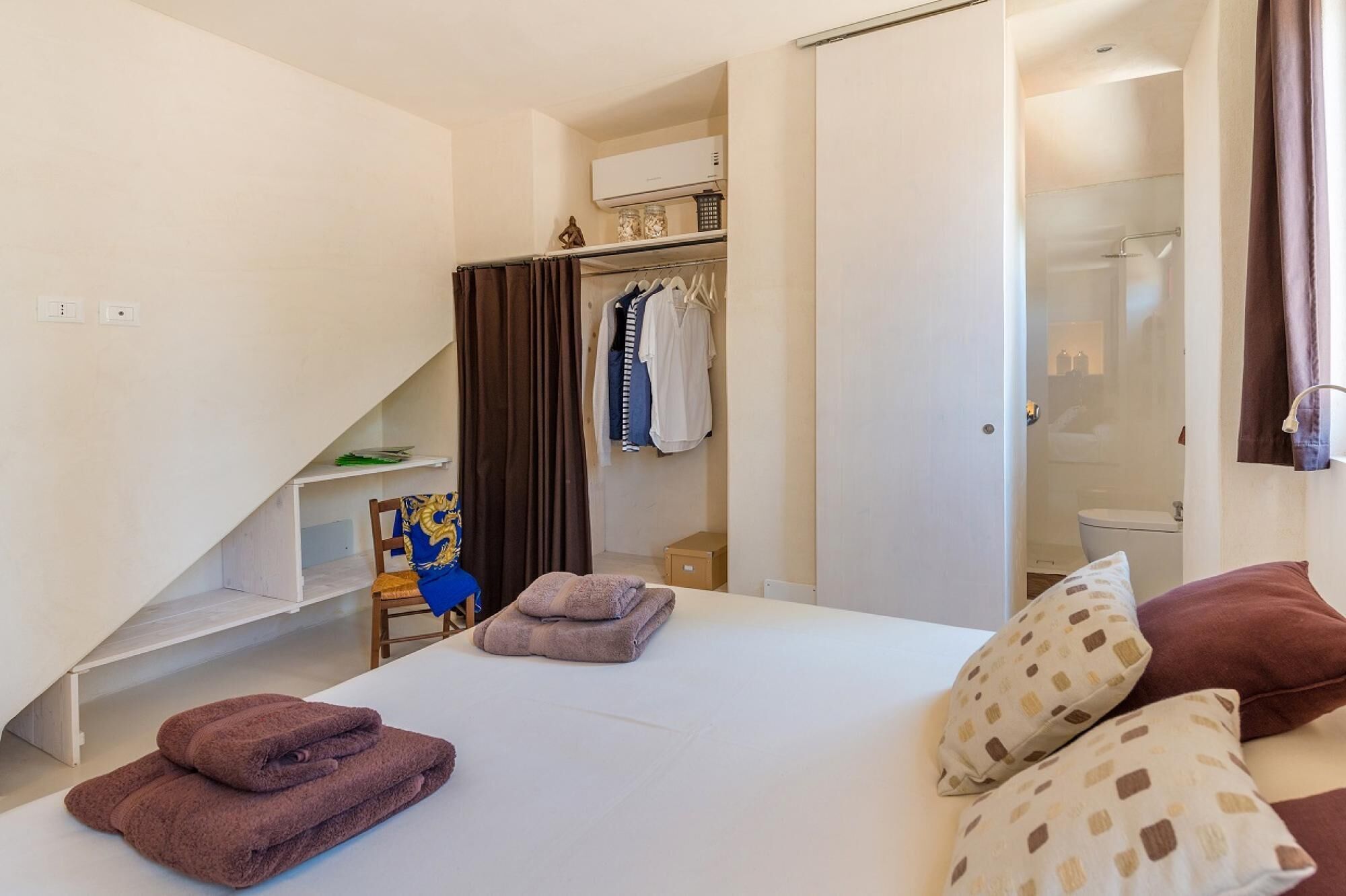 Una habitación de hotel con cama, armario, baño y una pequeña mesa con silla.