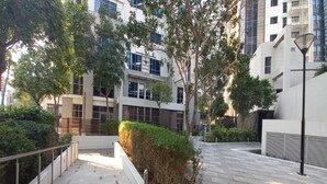 A modern urban courtyard with a paved walkway, surrounded by buildings with large windows and a street lamp. - Executive Towers Amazing 1BR Onsite Pool Business bay (Dubai)