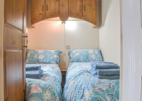 A compact bedroom with two beds, wooden cabinets, and a ceiling light fixture.
