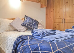 A neatly made bed with patterned bedding, a wooden wardrobe, and a light fixture above the bed. - Traditional yet comfortable caravan with one double and one twin. (Dolgellau)