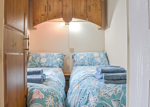 Quarto compacto com duas camas, armários de madeira e luminária no teto.