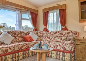 A cozy RV interior with a patterned sofa, a small round table with mugs, and a wooden cabinet. - Traditional yet comfortable caravan with one double and one twin. (Dolgellau)