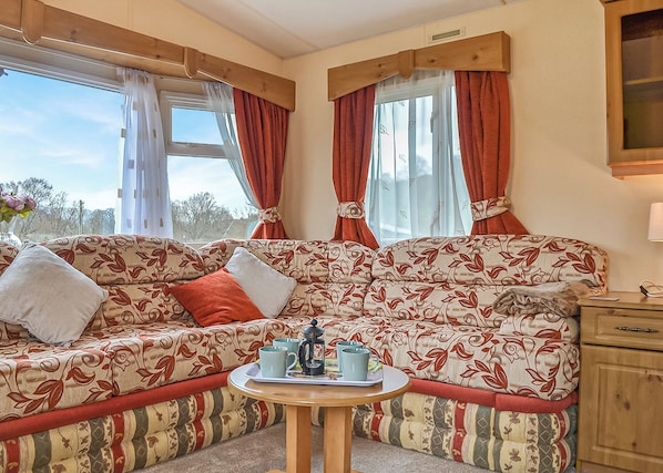 A cozy RV interior with a patterned sofa, a small round table with mugs, and a wooden cabinet.