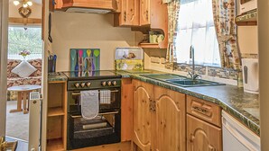 Una cocina con armarios de madera, estufa, lavamanos y ventana con cortinas.