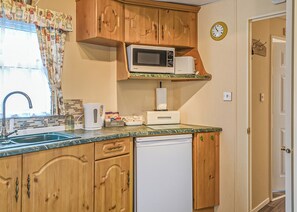 A compact kitchen with wooden cabinets, a microwave, a sink, and a dishwasher. - Traditional yet comfortable caravan with one double and one twin. (Dolgellau)