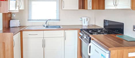 A compact kitchenette with a microwave, stove, sink, and a small refrigerator.