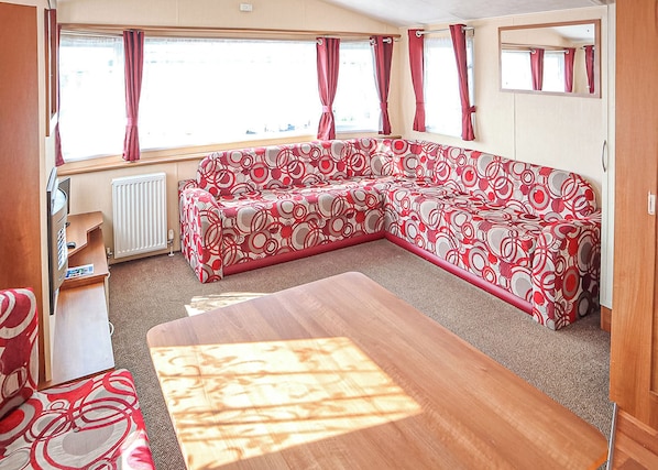 Ein Caravan-Innenraum mit einer Couch, einem Tisch, einem Heizkörper und Fenstern mit Vorhängen.