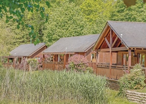 A row of log cabins with pitched roofs, wooden decks, and a natural backdrop.