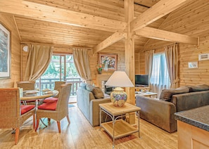A wooden cabin interior with a dining area, sofa, TV, and a fireplace.