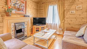 L’intérieur d’un chalet en bois comprend une cheminée, un téléviseur, un canapé et une table avec des magazines.