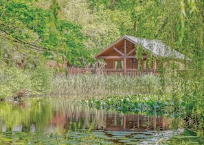 Una cabana de fusta amb teulada a dos vessants, envoltada per vegetació densa i una massa d'aigua plena de nenúfars.