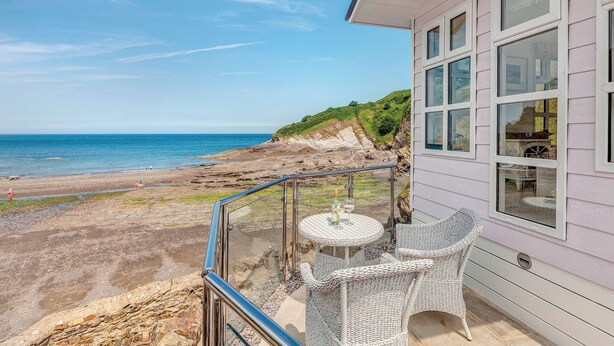 A balcony with wicker furniture overlooking a beach and ocean.