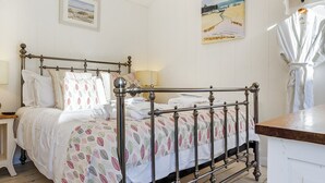 A neatly made bed with a patterned bedspread, a metal-framed four-poster bed, a bedside table with a lamp, and a framed picture on the wall.