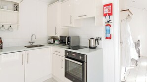 A modern kitchen with white cabinets, a sink, a toaster, a kettle, and a fire extinguisher. - Boutique style beach hut ideal for romantic getaways for all occasions. (Hele Bay, Ilfracombe)