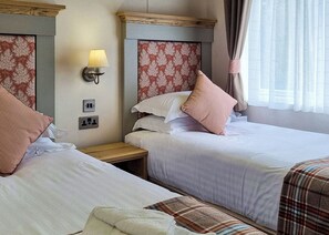 A hotel room with two beds, a nightstand, a lamp, and a power outlet.