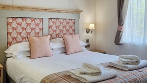 A neatly made bed with a plaid bedspread, two pink pillows, and a headboard with a floral pattern. - 1 bedroom accommodation in Woodhall Spa (Woodhall Spa)
