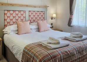A neatly made bed with a plaid bedspread, two pink pillows, and a headboard with a floral pattern.
