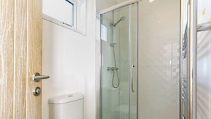 A bathroom with a toilet, a glass shower enclosure, and a wooden door. - Driftwood Beach Cabin (Hele Bay, Ilfracombe)