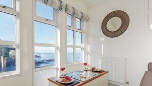 A room with large windows, a round mirror, and a table with food and drinks. - Driftwood Beach Cabin (Hele Bay, Ilfracombe)