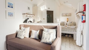 A modern interior with a sofa, a bed, a bathroom, and a kitchen area. - Driftwood Beach Cabin (Hele Bay, Ilfracombe)