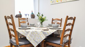 A dining table set with plates, bowls, and glasses, surrounded by wooden chairs with cushioned seats. - 1 bedroom accommodation in Dolgellau (Dolgellau)
