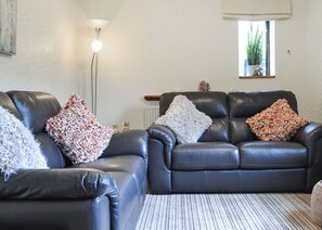 A living room with two black leather sofas, a striped rug, a floor lamp, and a window with a plant. - 2 bedroom accommodation in Dolgellau (Dolgellau)