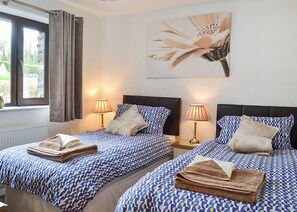 A hotel room with two beds, each with a patterned bedspread, bedside lamps, and a window with curtains. - 2 bedroom accommodation in Dolgellau (Dolgellau)