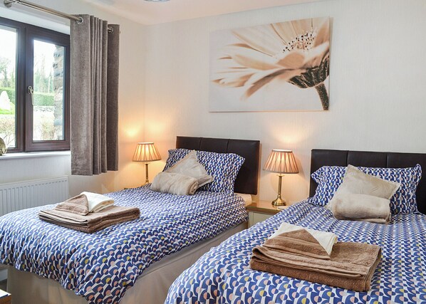 A hotel room with two beds, each with a patterned bedspread, bedside lamps, and a window with curtains.