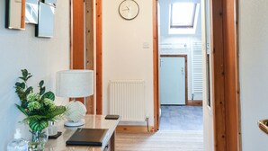 A hallway with a mirror, a clock, a radiator, a plant, a lamp, and a door leading to a room. - 1 bedroom accommodation in Dolgellau (Dolgellau)