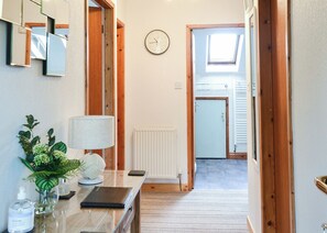 A hallway with a mirror, a clock, a radiator, a plant, a lamp, and a door leading to a room.