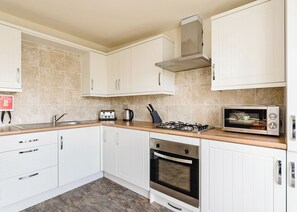 A kitchen with white cabinets, a gas stove, a microwave, and a sink. - Compact lodge finished to a high standard with one double and one with bunks. (Pickering)