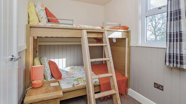 A bunk bed room with a ladder, a window with curtains, and a door.